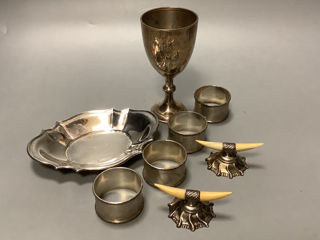 A set of four Edwardian engine turned silver napkin rings, Birmingham 1905, a pair of silver and Ivory mounted knife rests, a silver goblet and a silver dish.